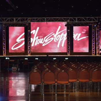 This is a photo representing a stage set-up with lighting and lit rectangular standing pillars in orange and blue around the front of the stage. 