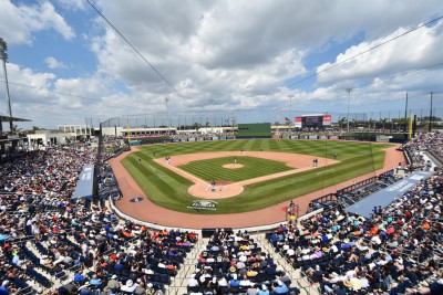 Panoramic view from behind home plate on a sunny day with a few clouds. A large audience and baseball players on the field.