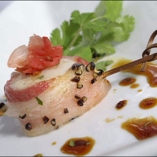 Food Photo of a bacon wrapped scallop with a decorative toothpick placed on a plate with parsley and pickled ginger garnish